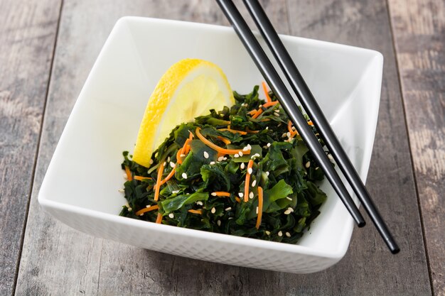 Salada wakame com cenoura, sementes de gergelim e suco de limão em uma tigela na mesa de madeira