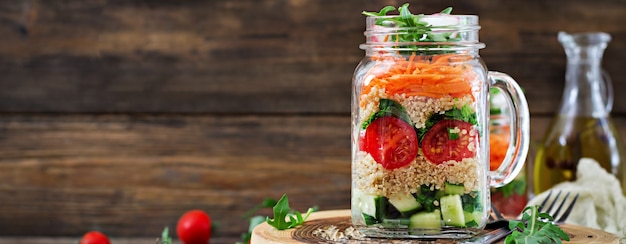 Saladas com quinoa, rúcula, rabanete, tomate e pepino em potes de vidro na mesa de madeira. comida saudável, dieta, desintoxicação e conceito vegetariano