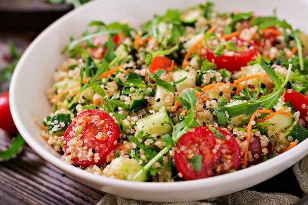 Foto saladas com quinoa, rúcula, rabanete, tomate e pepino em uma tigela na mesa de madeira. conceito de comida, dieta, desintoxicação e vegetariano saudável.