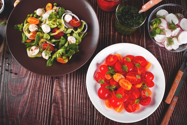 Saladas de tomate cereja fresco com manjericão, mussarela, verduras e rabanete na mesa de jantar