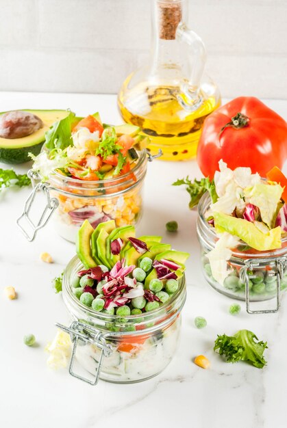 Saladas frescas em jar com legumes frescos e molhos saudáveis, na mesa de mármore branca, copie o espaço