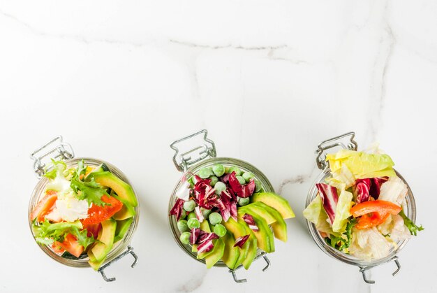 Saladas frescas em jarra com legumes frescos e molhos saudáveis, na mesa de mármore branca,