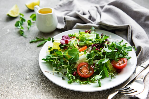 Saladeira verde fresca mista com tomates e microgreens na superfície de concreto