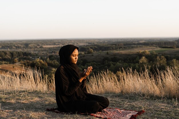 Salah tradicional orando a Deus no tapete. Mulher muçulmana negra orando a Alá.