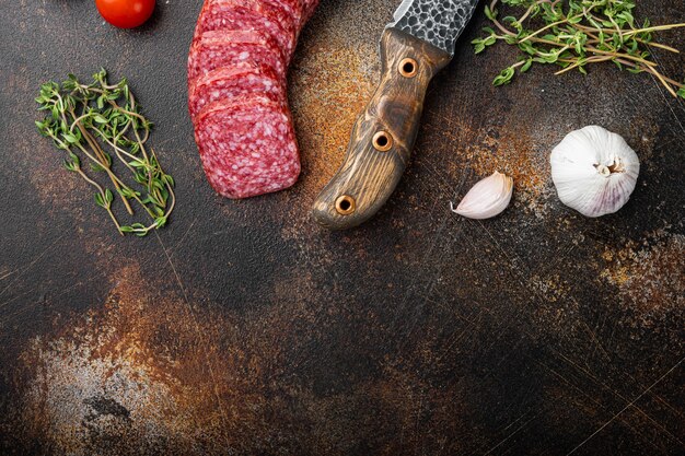 Salame com ervas, conjunto de alho, na velha mesa escura e rústica, vista de cima plana lay