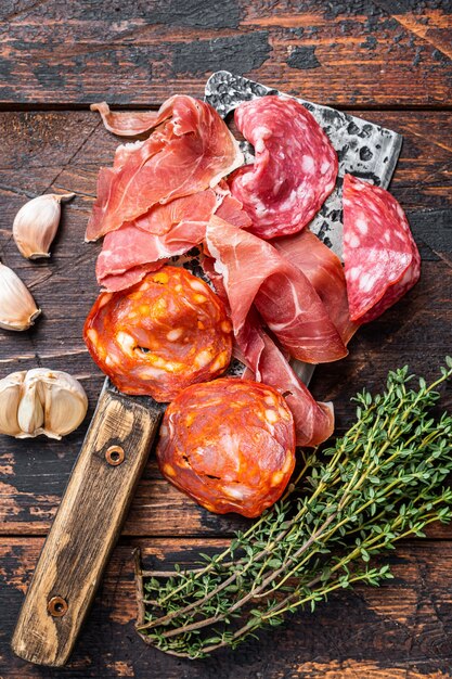 Salame de carne curada espanhola, jamon, salsichas curadas de choriso em um cutelo. Fundo de madeira escuro. Vista do topo.