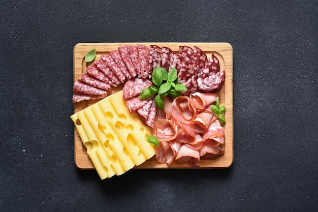 Salame de presunto de queijo em uma placa quadrada de madeira em um fundo de pedra preta delicadeza