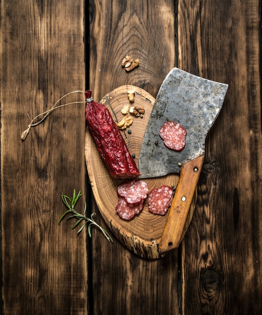 Salame e uma velha machadinha com alecrim. em fundo de madeira.