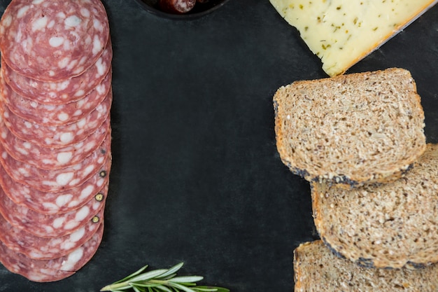 Salame, queijo e fatias de pão integral na placa de ardósia