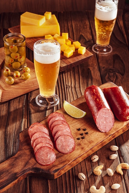 Salami ahumado en lonchas con dos vasos de cerveza, cubitos de queso, aceitunas, castañas y pistachos