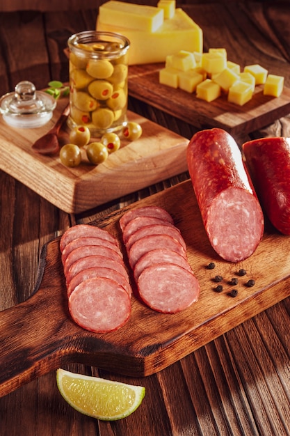 Salami ahumado en rodajas sobre tabla de cortar con cubitos de queso y aceitunas