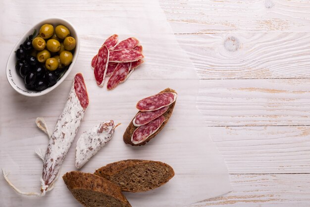 Salami und Brot auf weißem hölzernem Hintergrund. Ansicht von oben.