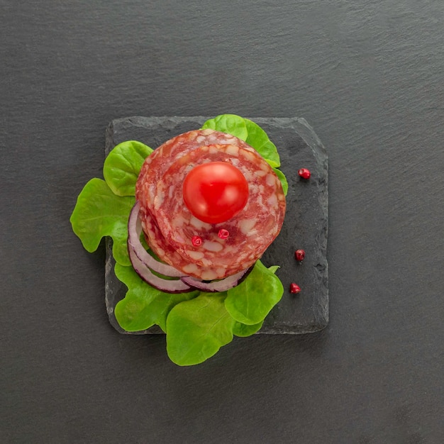 Salamiwurst isst auf einer schwarzen Schieferplatte mit Salatgewürzen und Tomaten Draufsicht Platz für Text