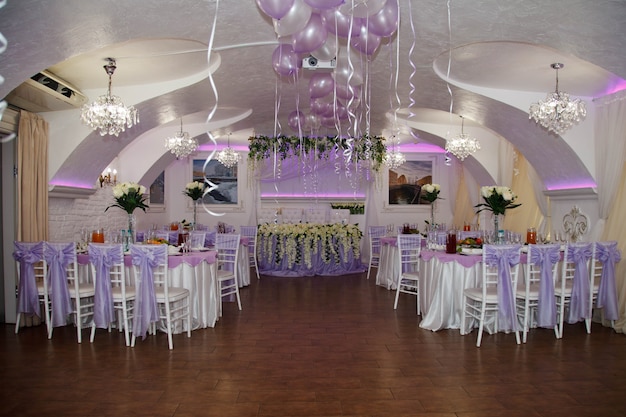 Salão coberto para recepções de casamento com mesas e decorações florais. Restaurante de celebração para noivos e convidados. Interior com design incrível. Design de luxo para eventos. Espaço de direitos autorais para o site