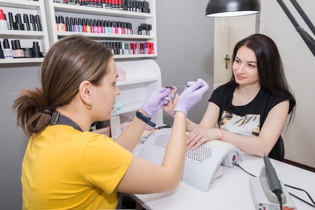 Foto salão de beleza. o mestre usa uma lima de unha para modelar as unhas durante a manicure. a menina é mestre e cliente de um salão de beleza.