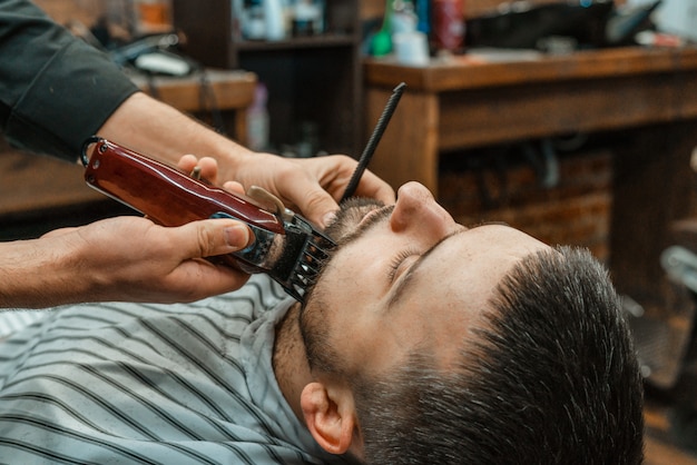 Salão de beleza para homens. barbear uma barba em uma barbearia. barber corta a barba com uma navalha e uma tesoura. close-up cortes de cabelo brutais. equipamento de cabeleireiro. foco seletivo.