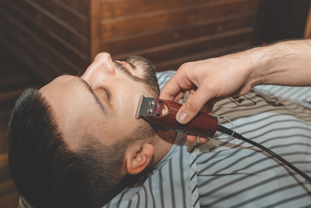 Salão de beleza para homens. Barbear uma barba em uma barbearia. Barber corta a barba com uma navalha e uma tesoura. close-up cortes de cabelo brutais. Equipamento de cabeleireiro. Foco seletivo.