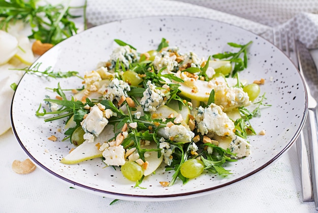 Salat aus Birne, Blauschimmelkäse, Traube, Rucola und Nüssen mit würzigem Dressing auf hellem Hintergrund. Gesundes Essen.