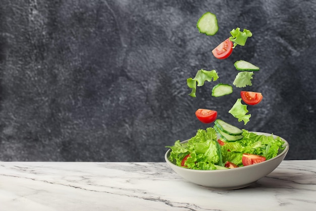 Salat aus frischem grünem Gemüse, der auf grauem Hintergrund in einen Teller fällt