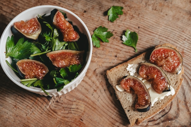 Salat aus frischen Feigen und Kräutern in einer weißen Schüssel auf einem hölzernen Hintergrund. Toast mit Käse und Feigen. Ein gesunder grüner Salat und ein frischer Obst- und Gemüsesnack.