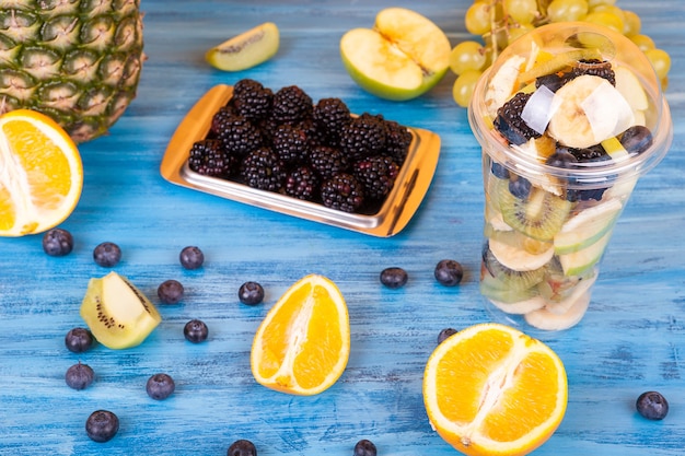 Salat aus frischen Früchten in einem Plastikbecher auf Holztisch geschnitten. Köstliches farbenfrohes Sommer-Früchte-Dessert