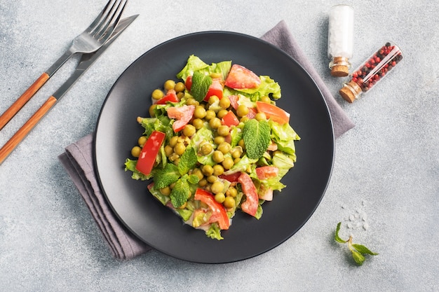 Salat aus grünen Tomatenblättern und Erbsen in Dosen, gewürzt mit Sauce auf einem schwarzen Teller. Frühlingsfrischer Diät-Salat. Draufsicht