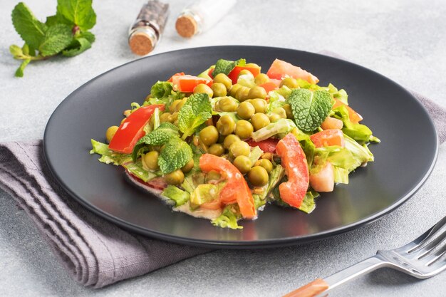 Salat aus grünen Tomatenblättern und Erbsenkonserven, gewürzt mit Soße auf einem schwarzen Teller. Frühlingsfrischer Diätsalat. Ansicht von oben