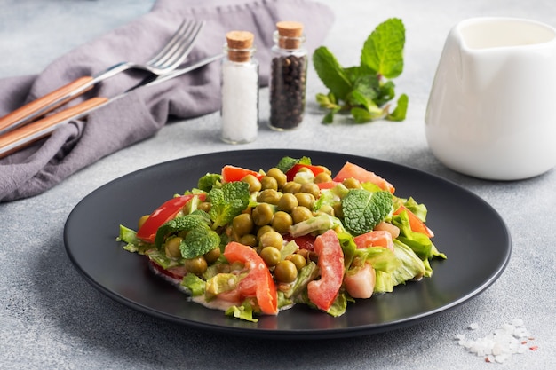 Salat aus grünen Tomatenblättern und Erbsenkonserven, gewürzt mit Soße auf einem schwarzen Teller. Frühlingsfrischer Diätsalat.