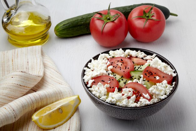 Salat aus Gurken, Tomaten mit Quark und Schwarzkümmel, gekleidet mit Olivenöl und Zitronensaft Schüssel mit frischem Gemüsesalat auf weißem Holztisch