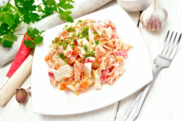 Salat aus Krabbenstäbchen, Käse, Knoblauch und Tomaten mit Mayonnaise-Tuch und Petersilie auf Holzbretthintergrund