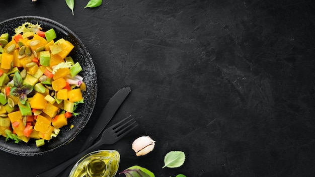 Salat aus Kürbis Avocado und Kürbiskernen auf schwarzem Hintergrund Ansicht von oben Freier Platz für Ihren Text