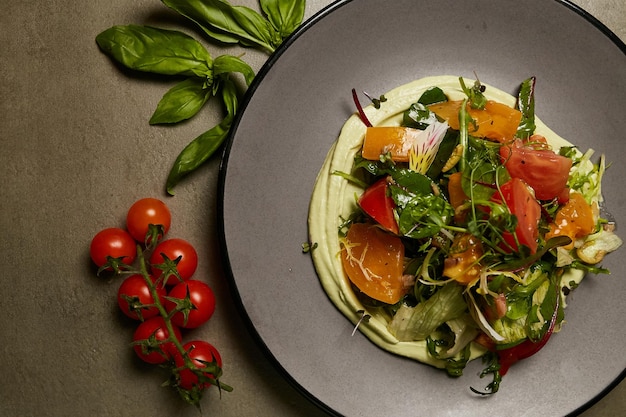 Salat aus Paprika-Tomaten-Kräutern und Kopfsalat auf einem grauen Teller