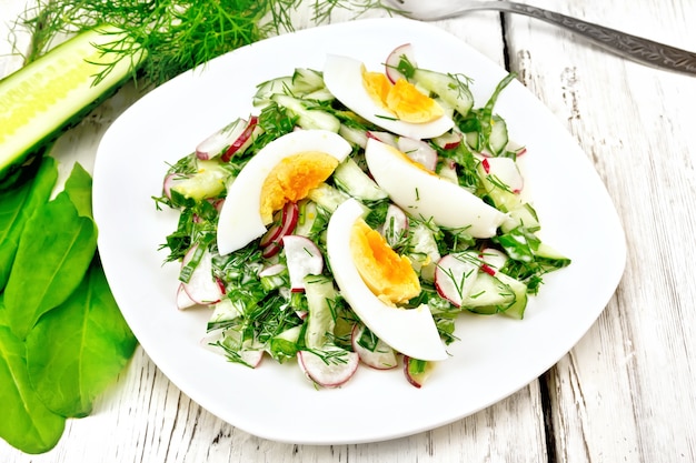 Salat aus Rettich, Gurke, Sauerampfer, Gemüse und Eiern, gekleidet mit Mayonnaise und Sauerrahm in einem Teller auf dem Hintergrund von Holzbrettern