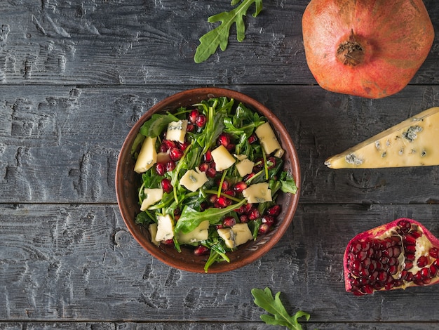 Salat aus Rucola, Granatapfel und Käse mit Blauschimmel auf einem rustikalen Tisch. Diät-vegetarischer Salat. Flach liegen.