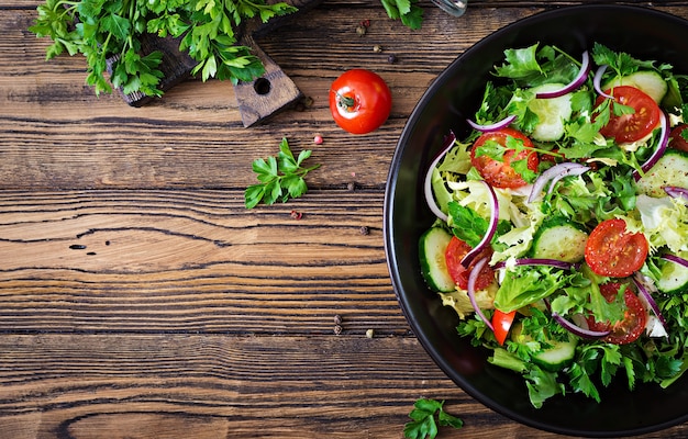 Salat aus Tomaten, Gurken, roten Zwiebeln und Salatblättern. Gesundes Sommer-Vitamin-Menü. Vegane Gemüsenahrung. Vegetarischer Esstisch. Ansicht von oben. Flach liegen