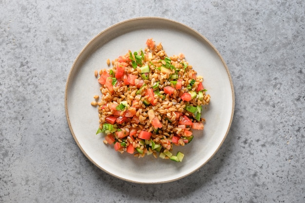 Salat aus Vollkorngetreide mit Gemüse auf grauem Tisch.