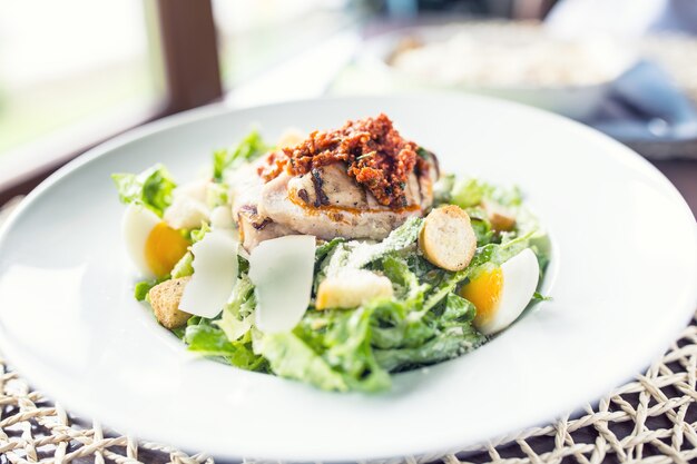 Salat Caesar mit gegrillten Hähnchenbruststücken auf weißem Teller im Restaurant.