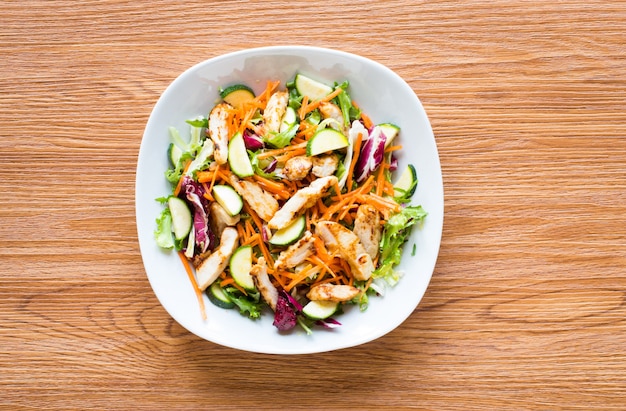 Salat der Hühnerbrust mit Zucchini- und Kirschtomaten, auf einem Holztisch