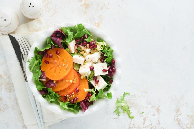 Salat Frischer grüner Salat mit Feta-Käse, Persimone, Granatapfel und Pistazien auf weißem Teller Idee für einen gesunden, köstlichen Winter-Weihnachtssalat Gesunde, ausgewogene Ernährung Draufsicht