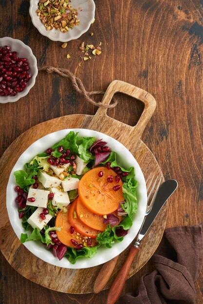 Salat Frischer grüner Salat mit Feta-Käse, Persimone, Granatapfel und Pistazien auf weißem Teller Idee für einen gesunden, köstlichen Winter-Weihnachtssalat Gesunde, ausgewogene Ernährung Draufsicht