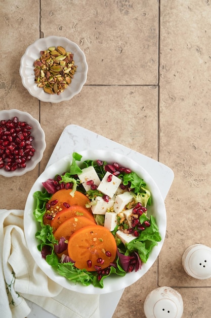 Salat Frischer grüner Salat mit Feta-Käse, Persimone, Granatapfel und Pistazien auf weißem Teller Idee für einen gesunden, köstlichen Winter-Weihnachtssalat Gesunde, ausgewogene Ernährung Draufsicht