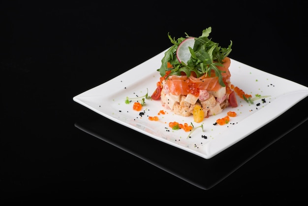 Salat in einem weißen quadratischen Teller auf schwarzem Hintergrund
