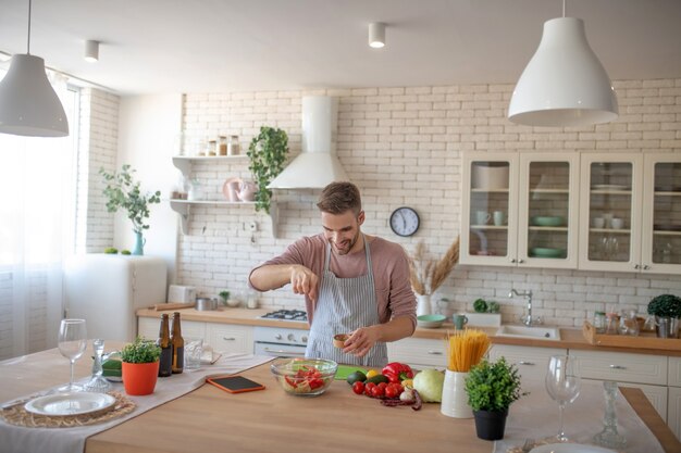 Salat kochen. Ein lächelnder Mann, der dem Gericht einige Gewürze hinzufügt