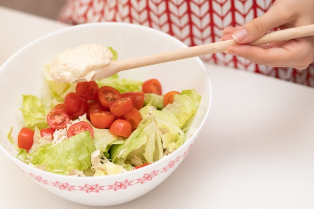 Salat kochen. Weibliche Hände geben die Sauce zu Caesar.