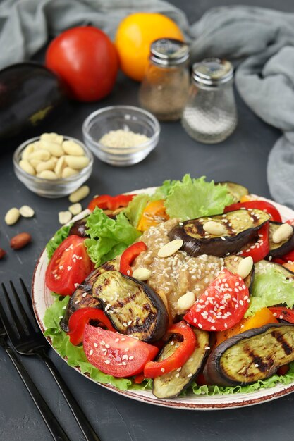 Salat mit Auberginen, Tomaten, Paprika, Salat, Sesam, Erdnusspaste Dressing auf dunklem Hintergrund
