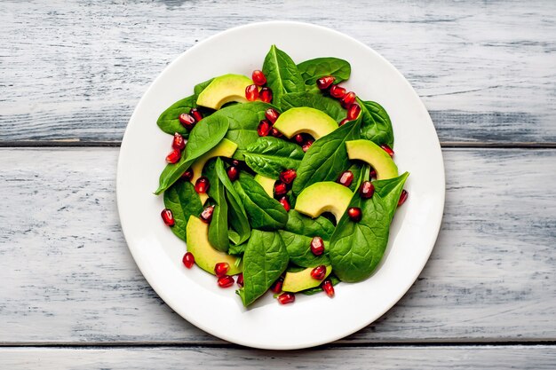 Salat mit Avocado, Rucola, Spinat, Granatapfel, Samen auf Holzhintergrund