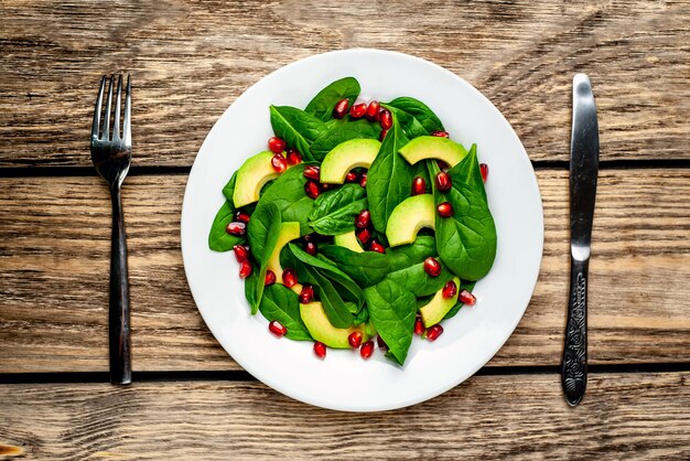 Salat mit Avocado, Rucola, Spinat, Granatapfel, Samen auf Holzhintergrund