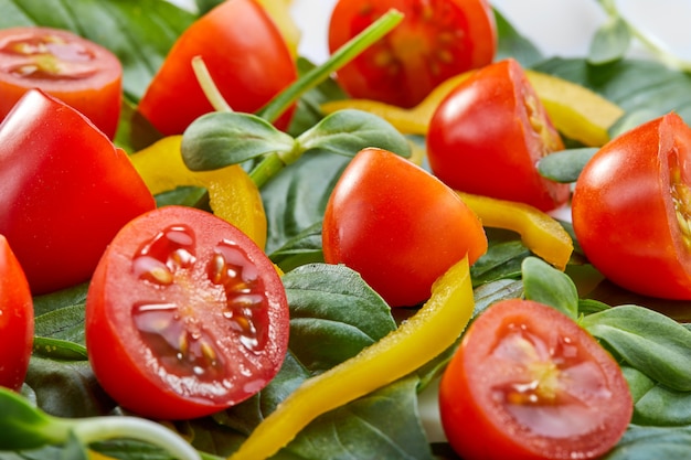 Salat mit Basilikumblättern, Kirschtomaten und grünem Pfeffer auf einer weißen Platte. Nahaufnahme, vorgewählter Fokus