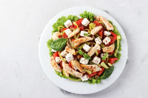 Salat mit Bulgur, gebackenem Huhn, Paprika, Basilikum und Feta auf einem weißen Teller, Draufsicht