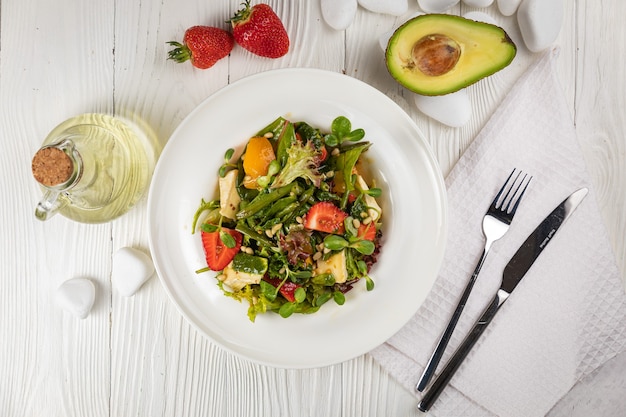 Salat mit Erdbeeren Brie-Käse-Tomaten und Gemüse auf einem weißen Teller und einem weißen Tisch